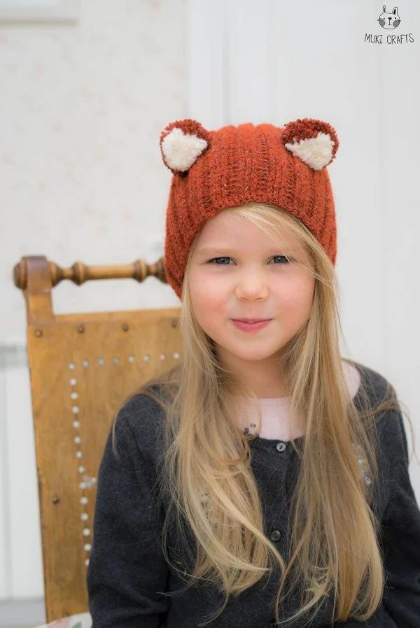 A young child wearing a fox-themed crochet animal hat.