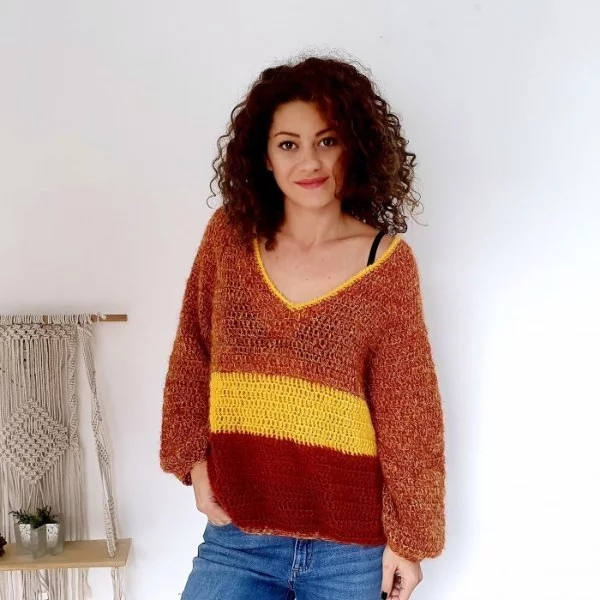 A woman wearing a v-neck sweater crocheted in fall colours.