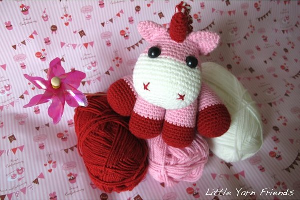 A crochet unicorn toy in shades of pink and red.