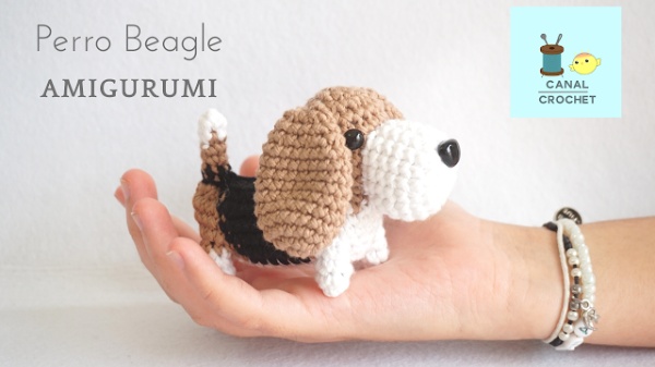 A crochet Beagle dog sitting in the palm of a hand.