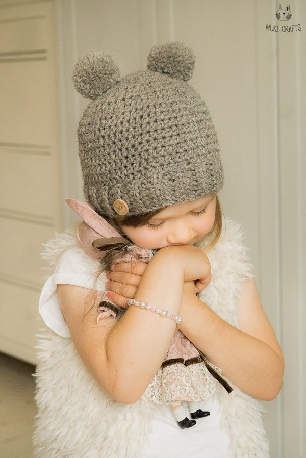 A little girl earing a crochet animal hat with pompom ears.