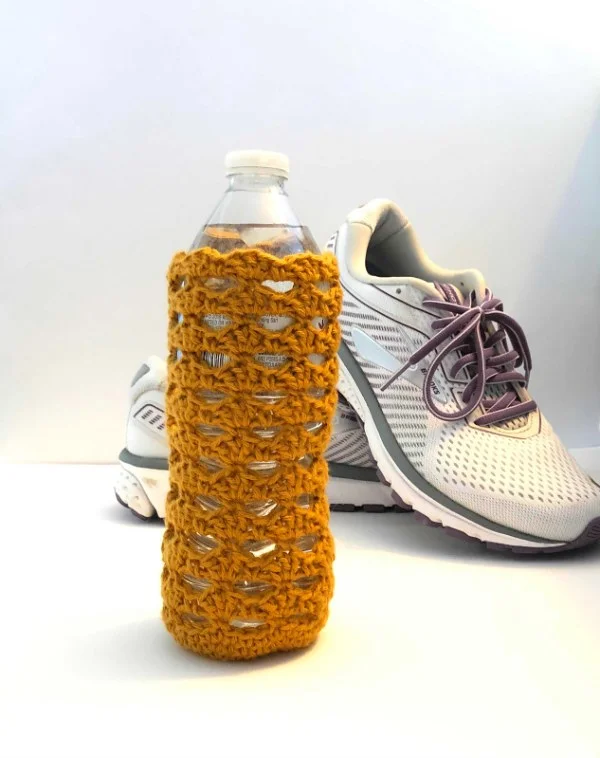 A mustard coloured crochet water bottle cozy.