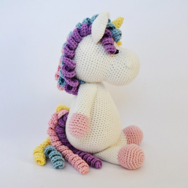 A crochet unicorn softie with curly rainbow hair and tail.
