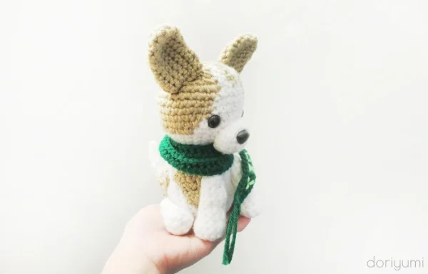 An amigurumi crochet Chihuahua wearing a grren scarf.