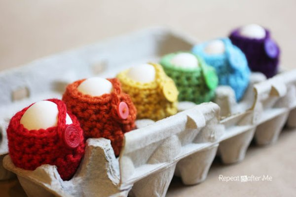 A carton of eggs each in a different coloured crochet egg cozy with buttons.