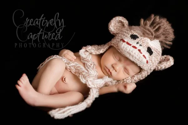 A newborn baby earing a crochet monkey hat.