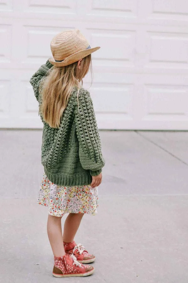 A child wearing a green, crochet hexagon cardigan.