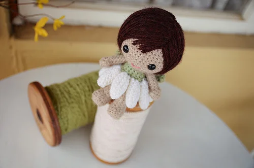 A tiny crochet fairy doll sitting on a spool of thread.