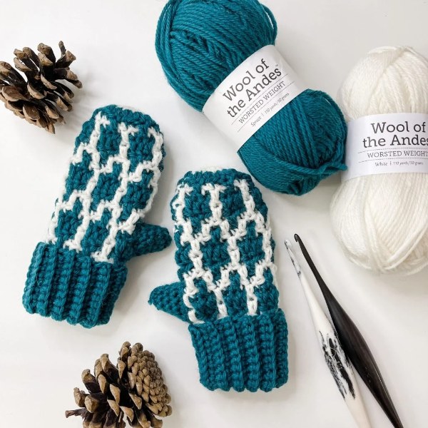 A pair of mosaic crochet kids mittens with yarn and a crochet hook.