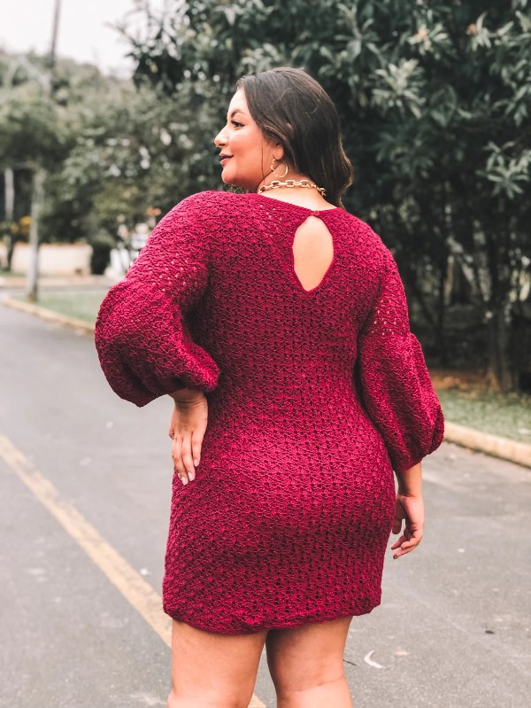 Back view of a wpman wearing a red crochet sweater dress with puff sleeves.