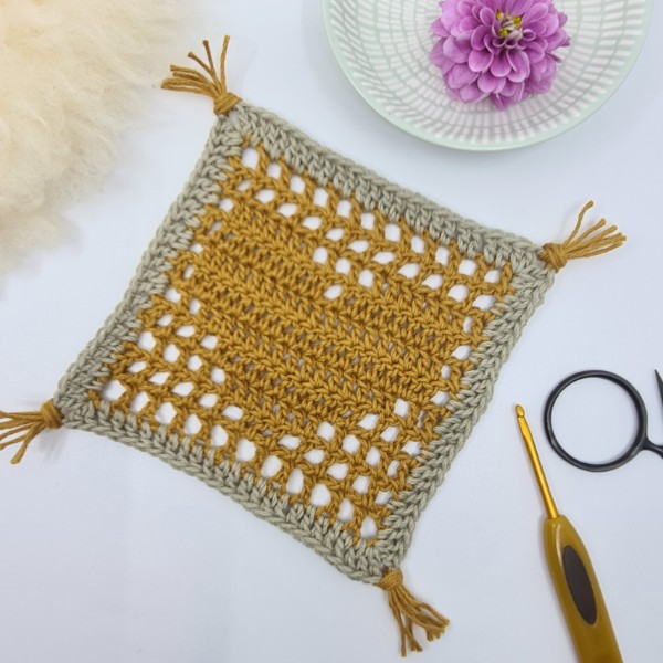 A yellow, filet crochet mug rug featuring a heart motif.