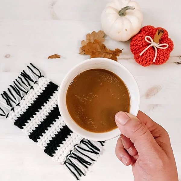 A black-and-white striped crochet mug rug and a cup of coffee.