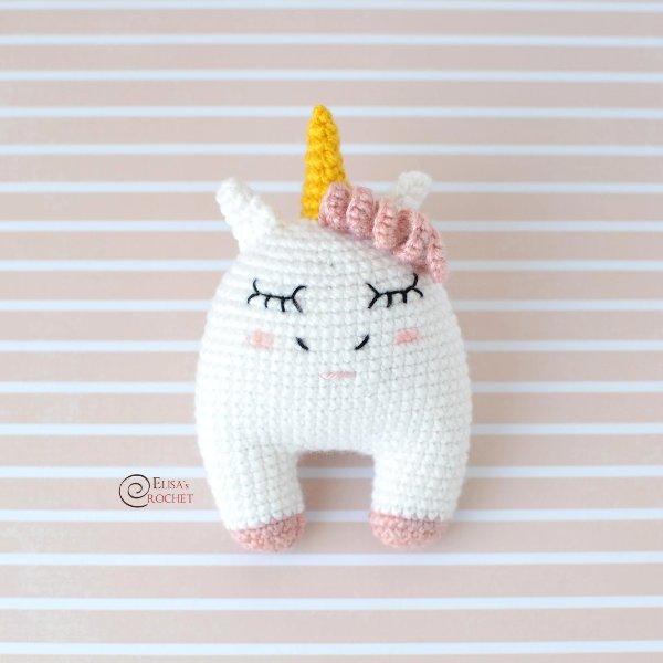 A simple crochet unicorn toy with pink hair and a golden yellow horn.
