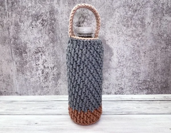 Two-colour, textured crochet water bottle holder with short handle.