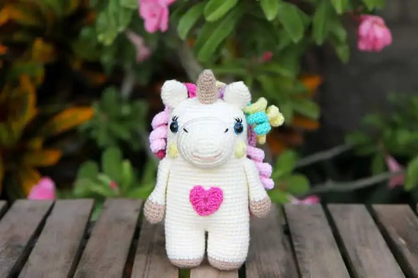 A crochet unicorn with rainbow hair and a loveheart detail.