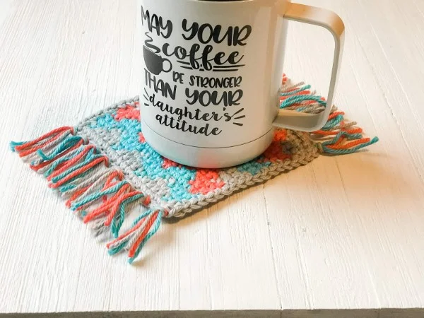 A colourful crochet mug rug featuring chevron zig zag stripes.