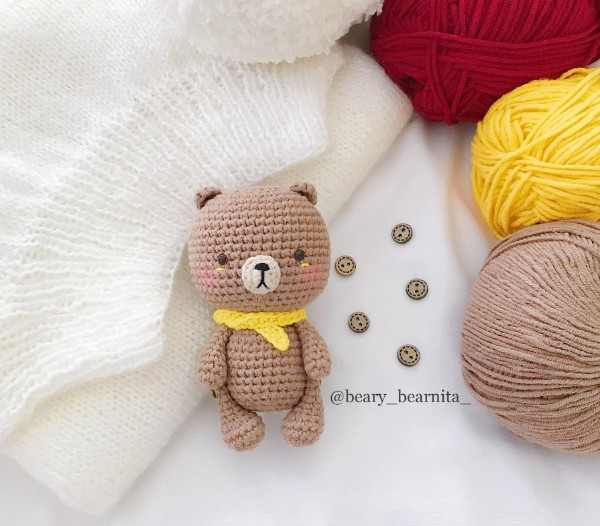 A small, crocheted baby bear with a yellow scarf.