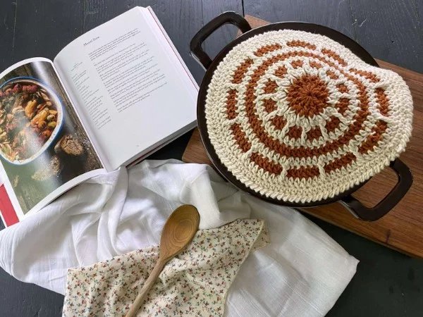 A crochet circle potholder with kitchen paraphernalia.