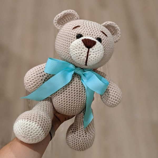 A classic looking crochet teddy bear with a big blue bow.