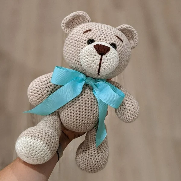 A classic looking crochet teddy bear with a big blue bow.