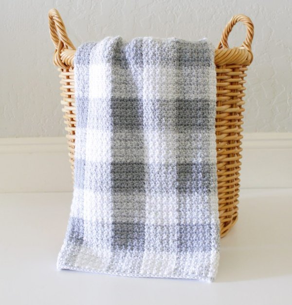 A grey gingham crochet blanket hanging over the side of a basket.