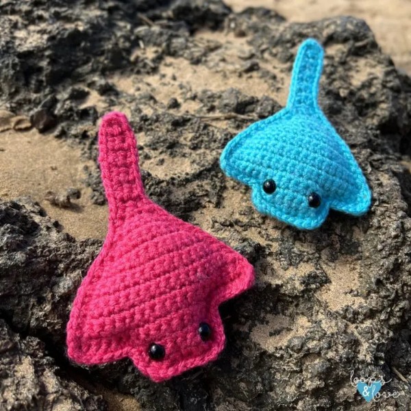 Two crochet stingray toys laying on a rocky beach.