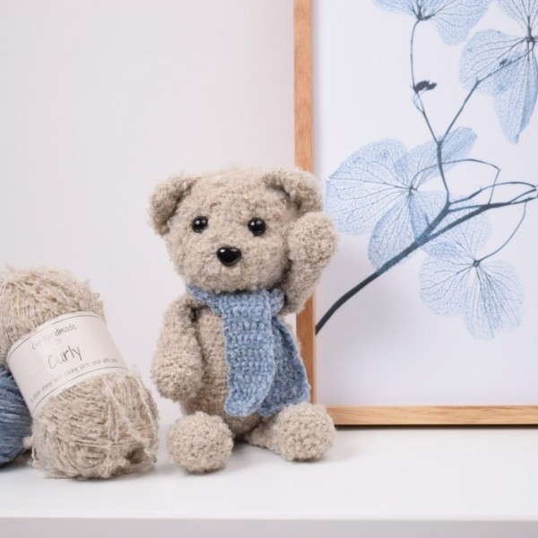 A crochet teddy bear with a blue scarf.