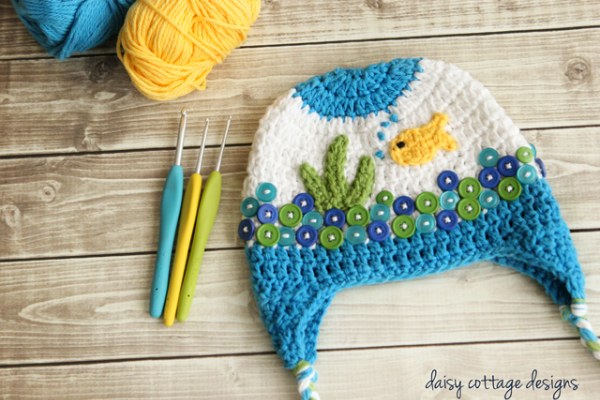 A crochetr earflap hat for babies with fishbowl-themed appliques.