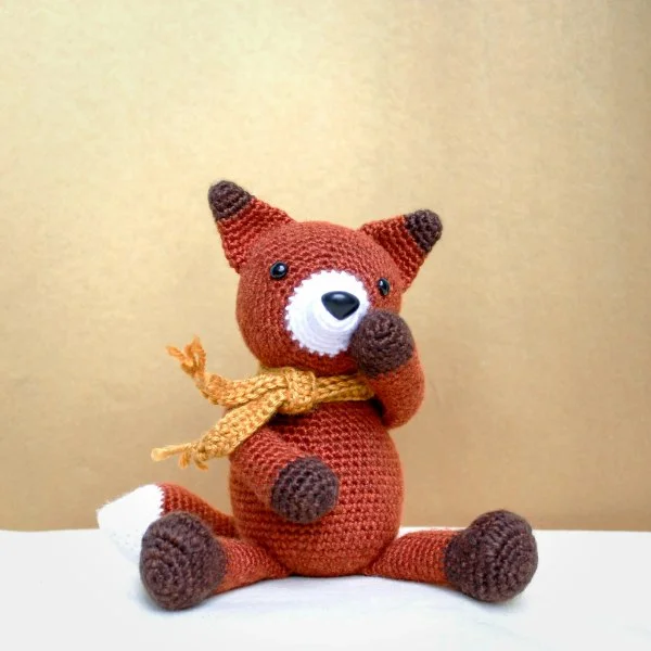 An amigurumi fox with a yellow scarf.