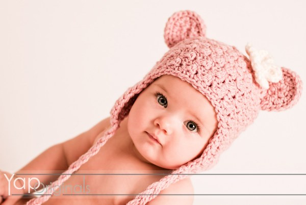 A baby wearing a pink crochet earflap hat with bear ears.