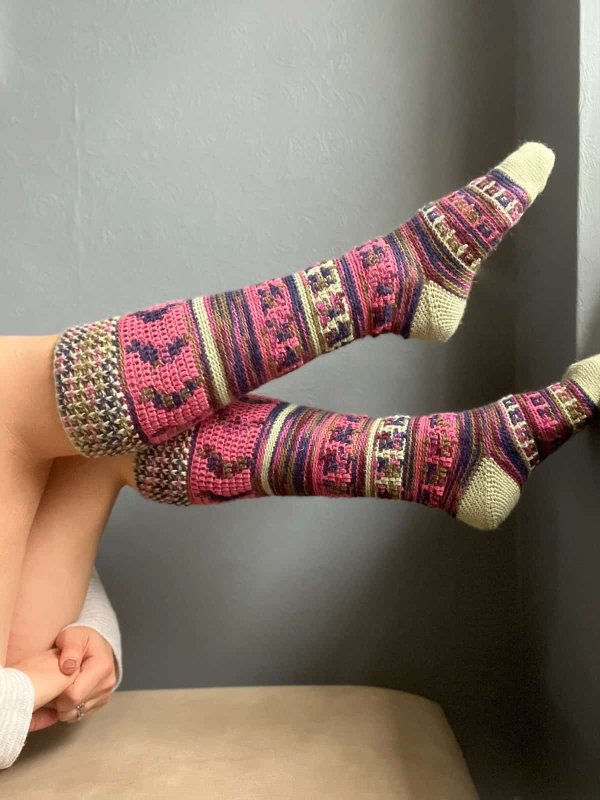 A closeup of a person's legs, wearing mosaic colourwork long crochet socks.