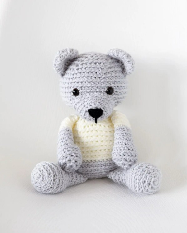 A grey crochet teddy bear with a white t-shirt.