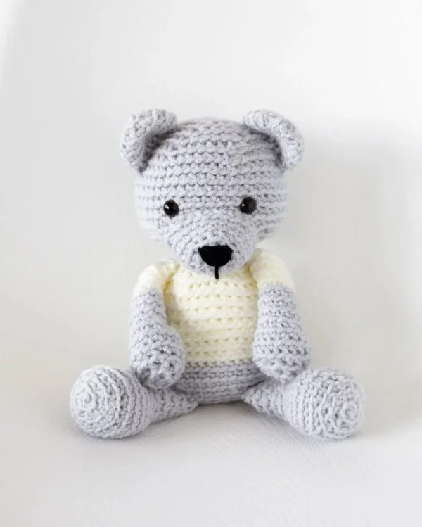 A grey crochet teddy bear with a white t-shirt.