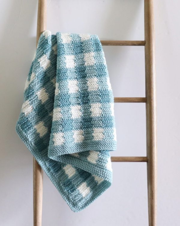 A teal blue crochet ginham blanket draped over a ladder.