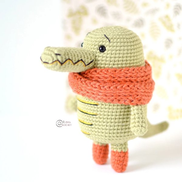 A standing crocodile amigurumi wearing a scarf.