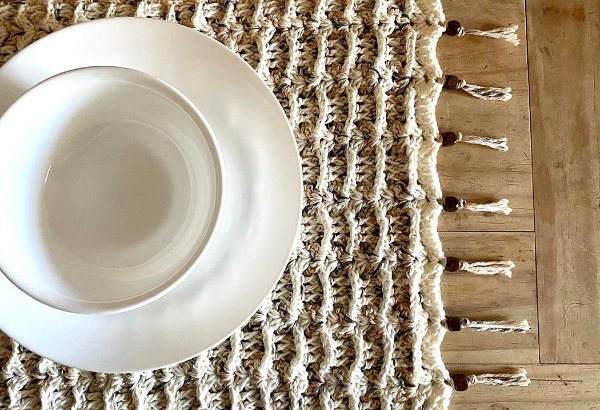 A bowl and plate on a textured crochet placemat with beaded tassels.