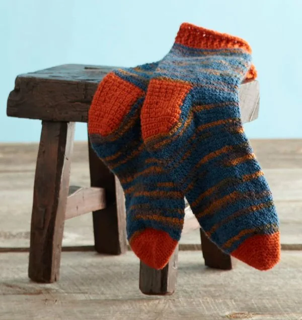 A pair of men's crochet socks on a wooden stool.