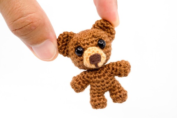 A tiny crochet bear held between two fingers.