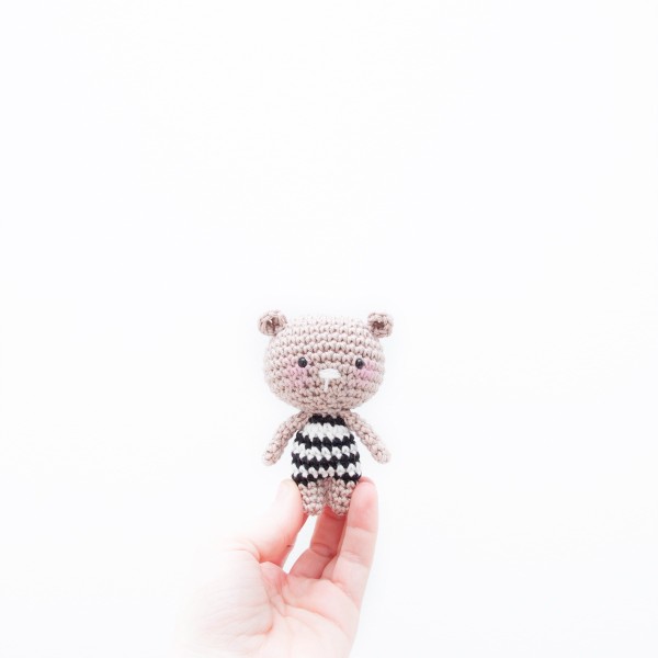 A tiny crochet bear wearing a black and white striped tee.