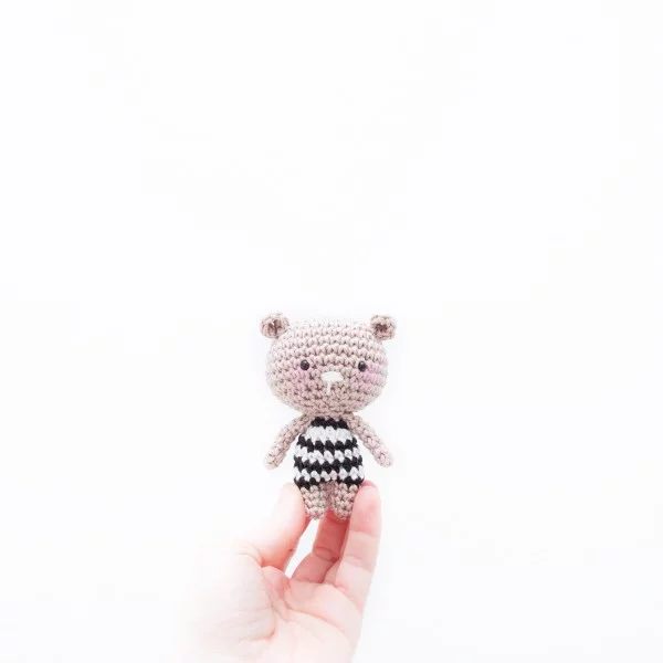 A tiny crochet bear wearing a black and white striped tee.