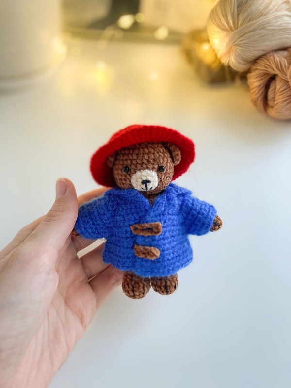 A crochet Paddington bear wearing a blue coat and a red hat.