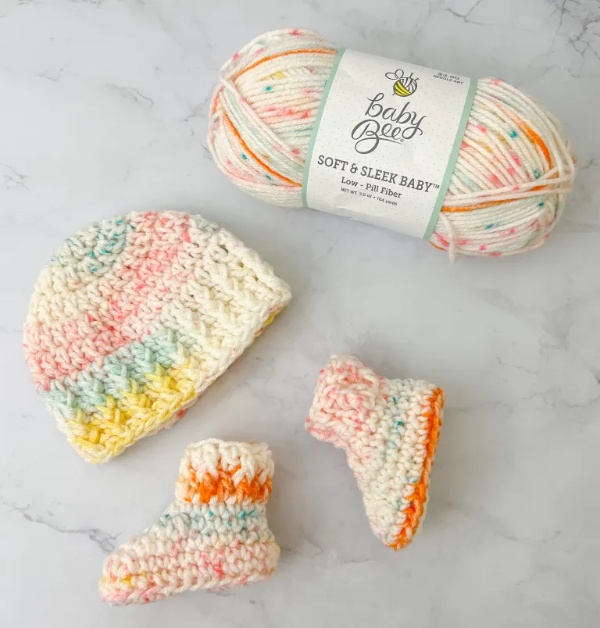 A newborn set of crochet baby booties and a hat next to a ball of yarn.
