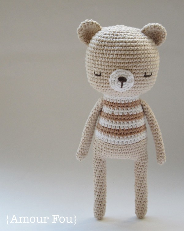 A crochet teddy bear with a striped t-shirt and long , skinny arms and legs.