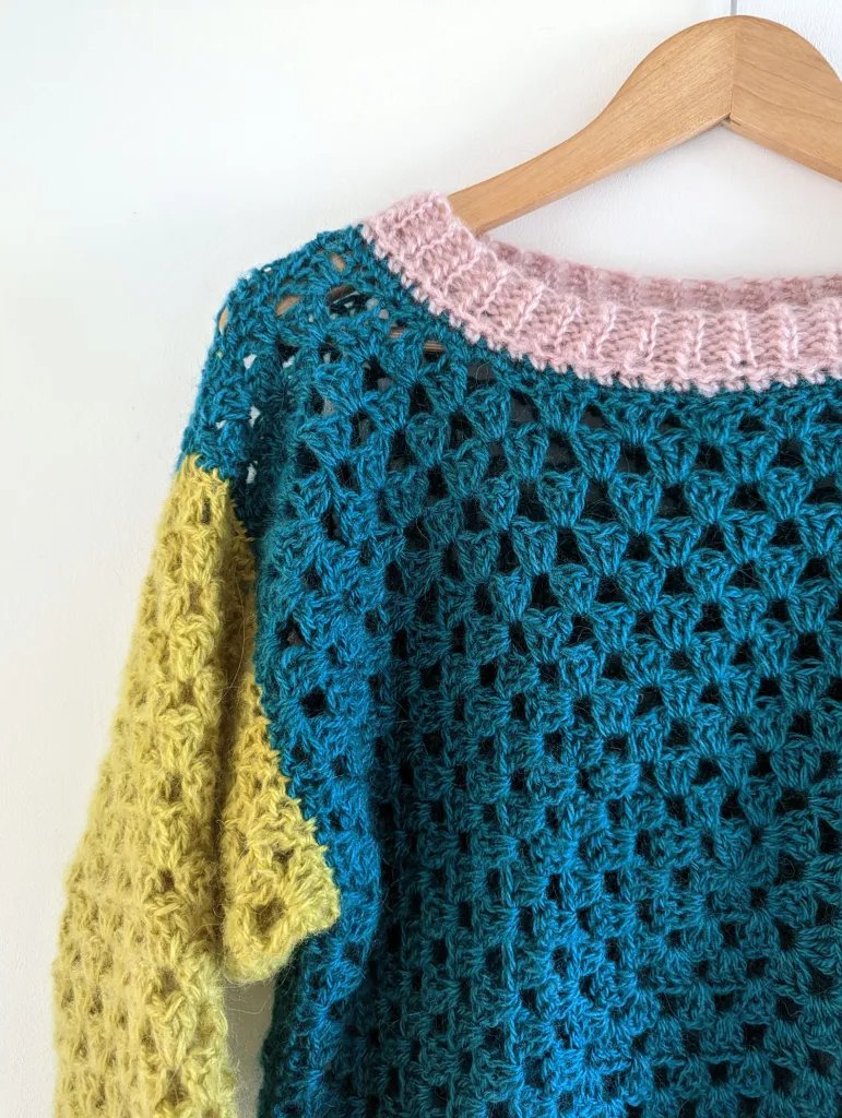 A colour blocked crochet granby square sweater on a wooden hanger.