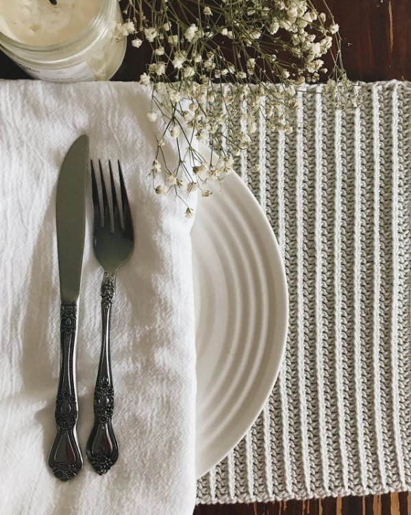 A rib stitch crochet placemat table setting with flowers and linen serviettes.