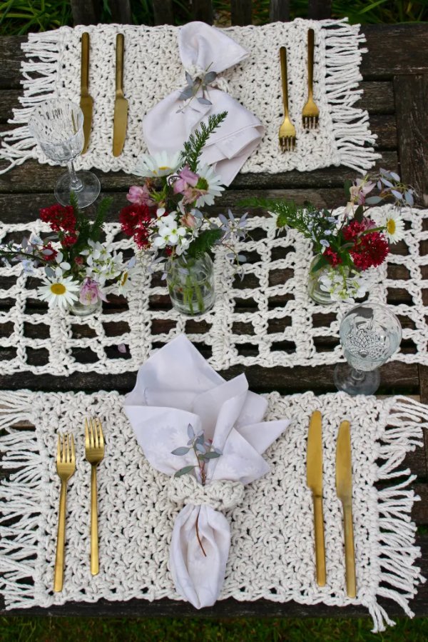 A boho-style outdoor table setting with crochet placemats and flowers.