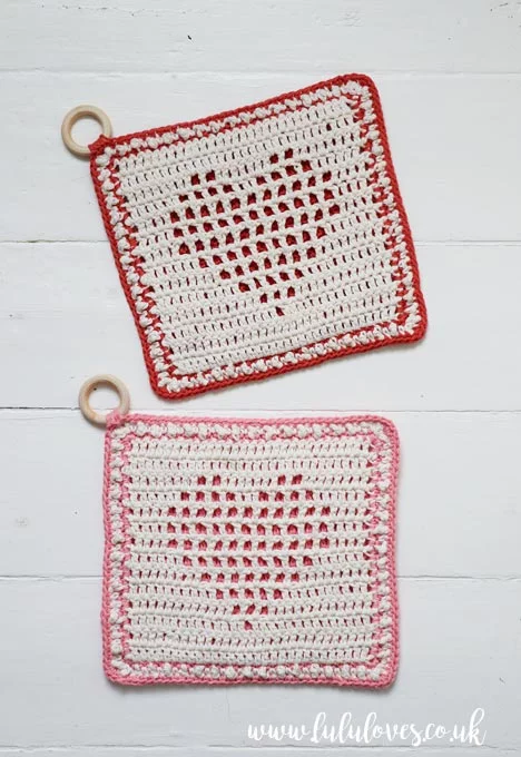 Two filet crochet potholders with centre heart motifs.