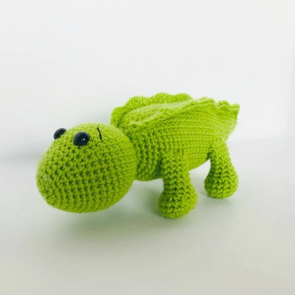 A bright green crochet alligator with a cute facial expression.