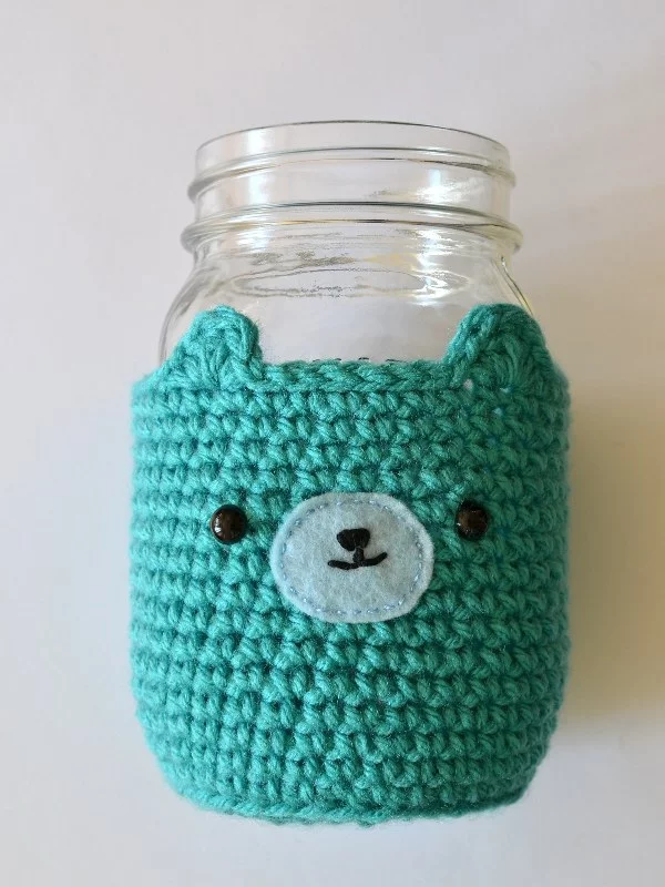 A blue crochet mason jar cover witha bear face.