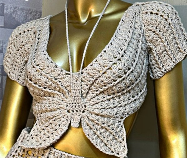 A gold mannequin dressed in a beige coloured crochet butterfly top.